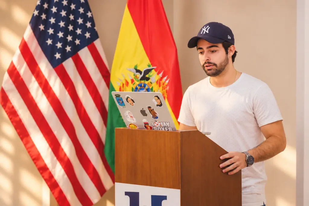 Alumno de iU presentando en clase frente a las banderas de Estados Unidos y Bolivia