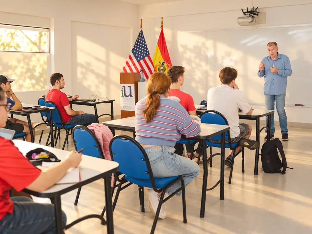Clase en iU: alumnos en un aula de Santa Cruz de la Sierra con las banderas de Estados Unidos y Bolivia