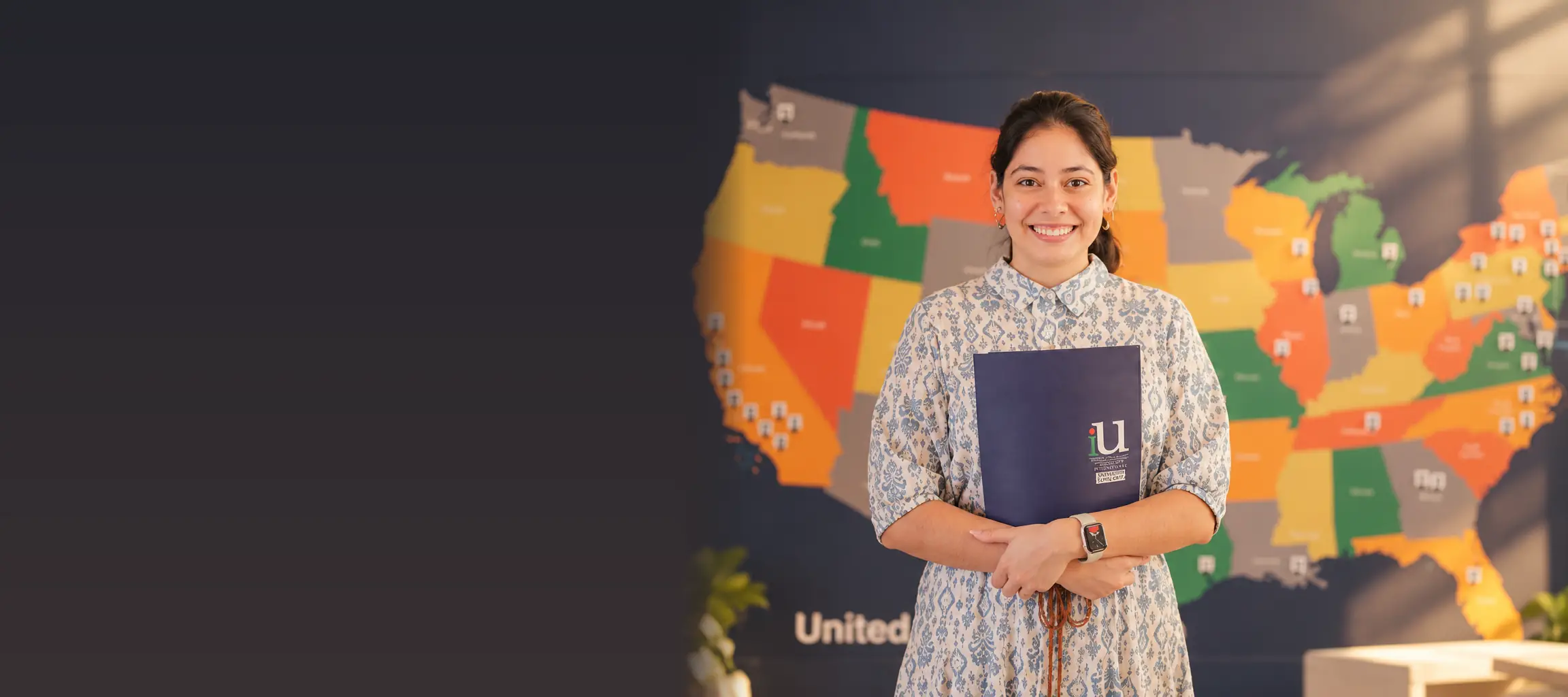 Alumna de iU con su carpeta frente al mapa de Estados Unidos en el campus de Santa Cruz de la Sierra